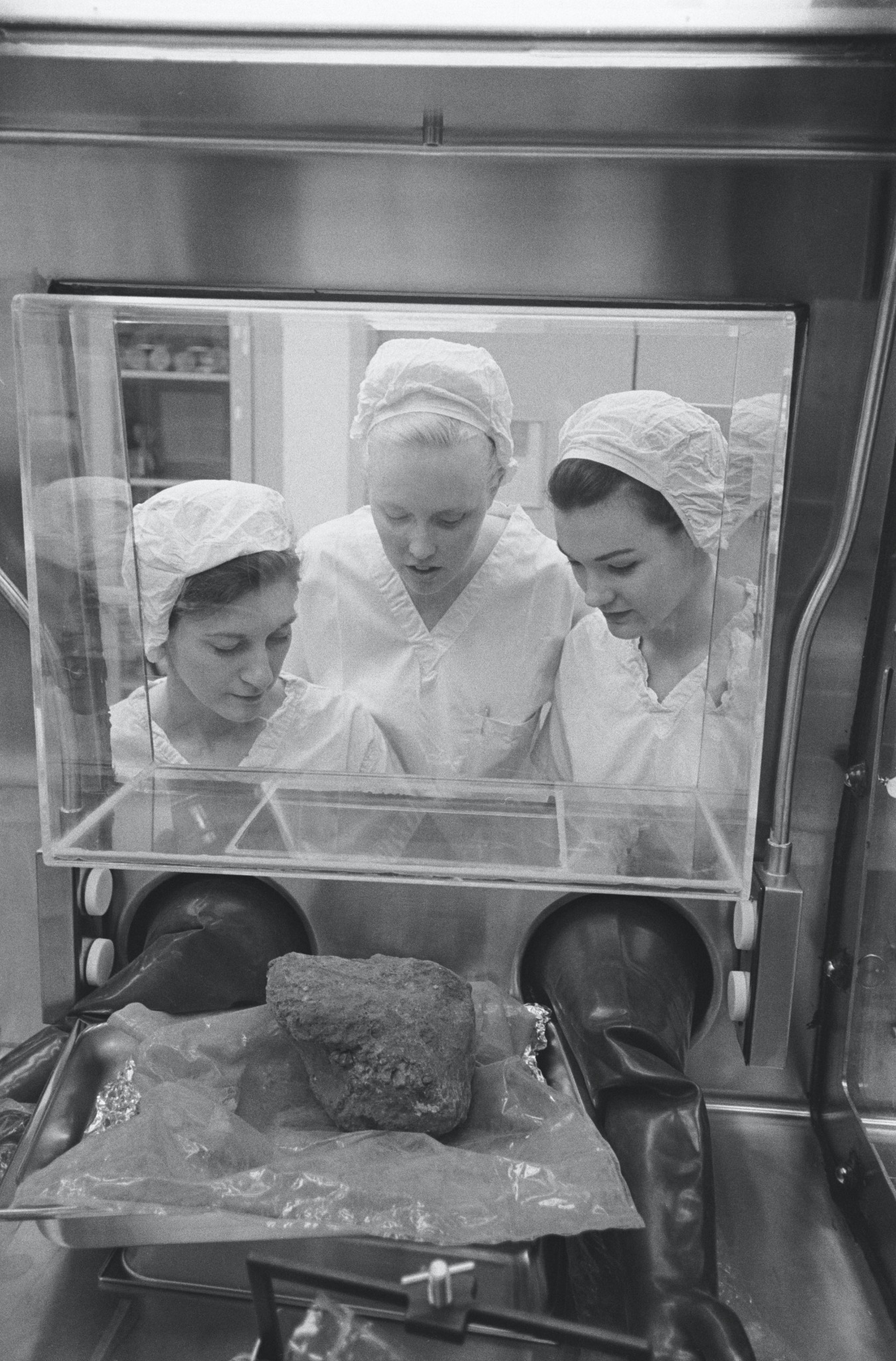 Researchers examining a lunar sample inside a protective laboratory cabinet